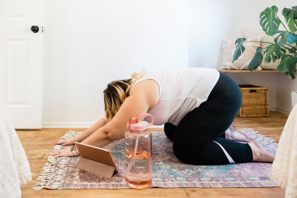 Frau in Yoga-Haltung auf Teppich mit iPad und Wasser